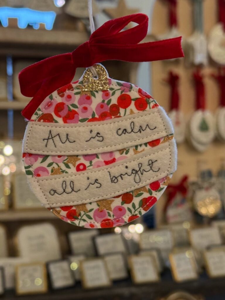 Fabric Christmas ornament with red bow and embroidered text hanging in a shop.