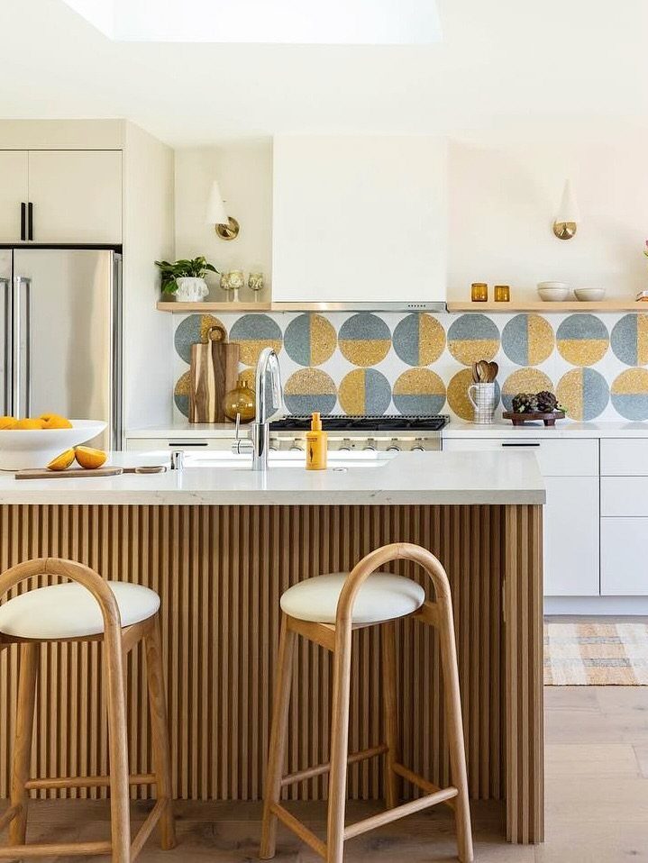 Modern kitchen with a wood slat island, geometric backsplash, and two wooden bar stools.