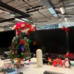 A small decorated Christmas tree with colorful lights sits on a white office desk.