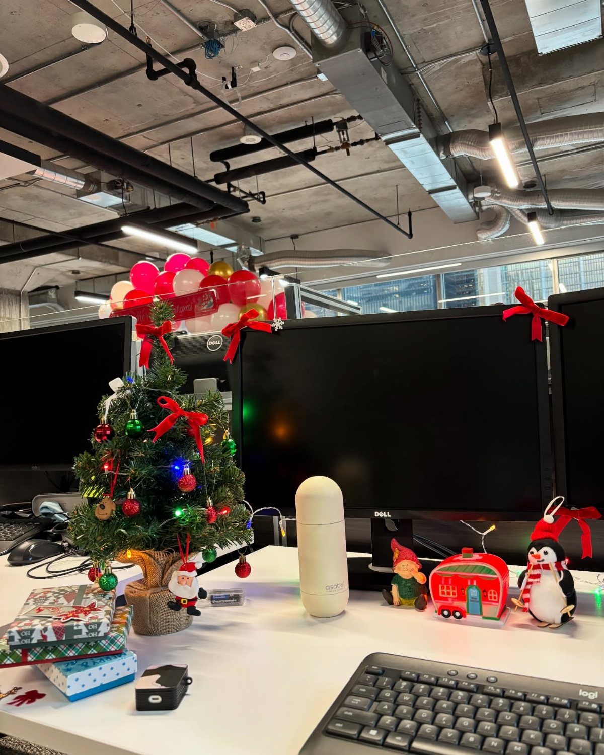 A small decorated Christmas tree with colorful lights sits on a white office desk.