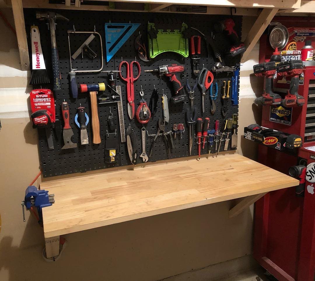 A wooden fold-down workbench mounted below a pegboard filled with various garage tools.